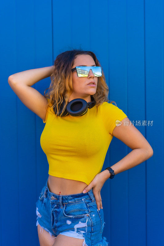 生活方式，金发白种人女孩黄色t恤蓝色背景。戴着耳机的Dj女孩为techno、house party或session海报做宣传